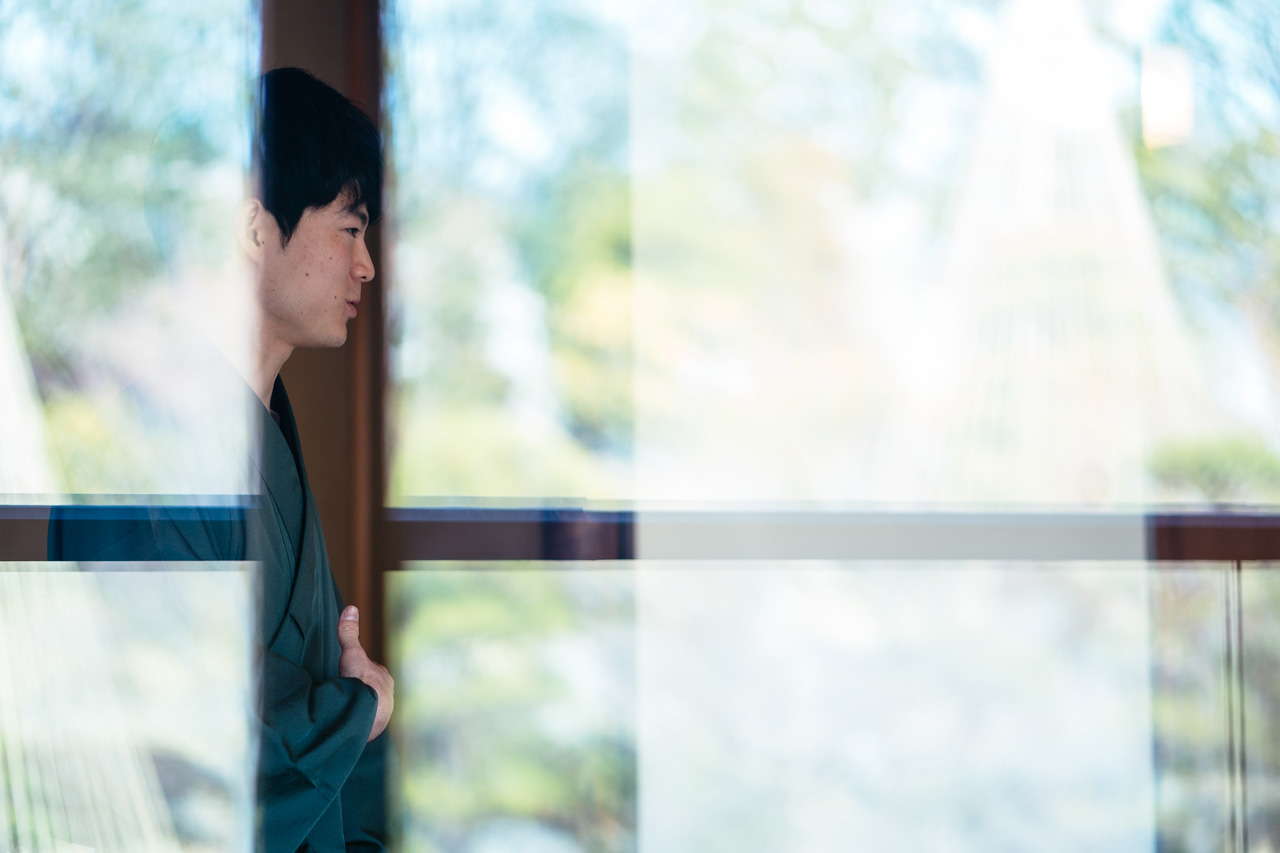 Ryo Iwamoto picture through a pane of glass, upon which the greenery from outside is reflected